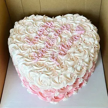 Heart-shaped cake with light pink and white frosting in a swirl pattern.