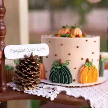 A pumpkin spice latte cake with pumpkin decorations and a sign. The cake is on a lace doily.