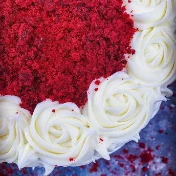 Red velvet cake with white frosting roses around the edge and red cake crumbs on top.