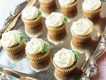 Mini cupcakes on a silver tray, frosted with white buttercream roses. Green frosting leaves decorate the base of the roses.