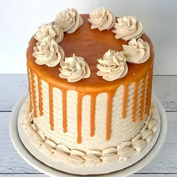Caramel cake with caramel drip and frosting rosettes. The cake is on a white cake stand.
