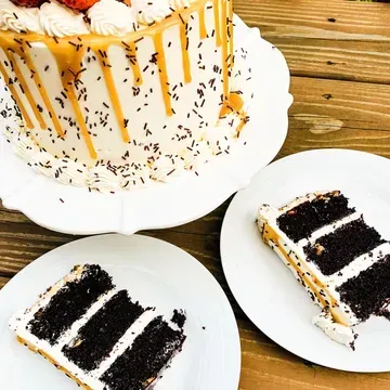 Chocolate cake with white frosting, caramel drizzle, and sprinkles, with two slices on plates.