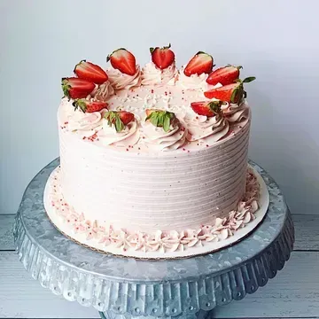 A pink frosted cake topped with strawberries on a silver cake stand.