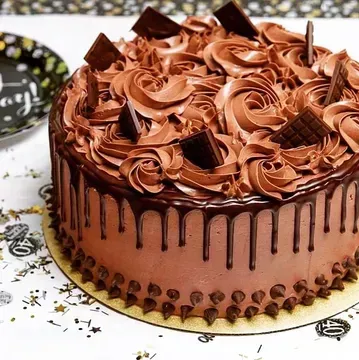 Chocolate cake with chocolate frosting, drips, and chocolate chunks. It is sitting on a golden base.