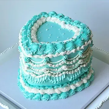 Heart-shaped cake decorated with turquoise and white frosting, silver sprinkles, and a blue heart center.