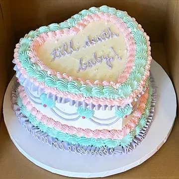 Heart-shaped cake with pastel frosting in pink, green, and purple, decorated with the phrase