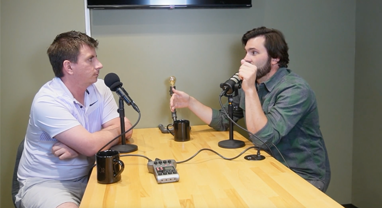 Two men are sitting at a table talking into microphones.