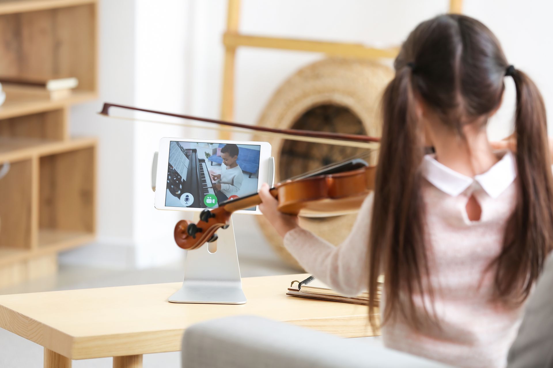 A little girl is playing a violin in front of a tablet.