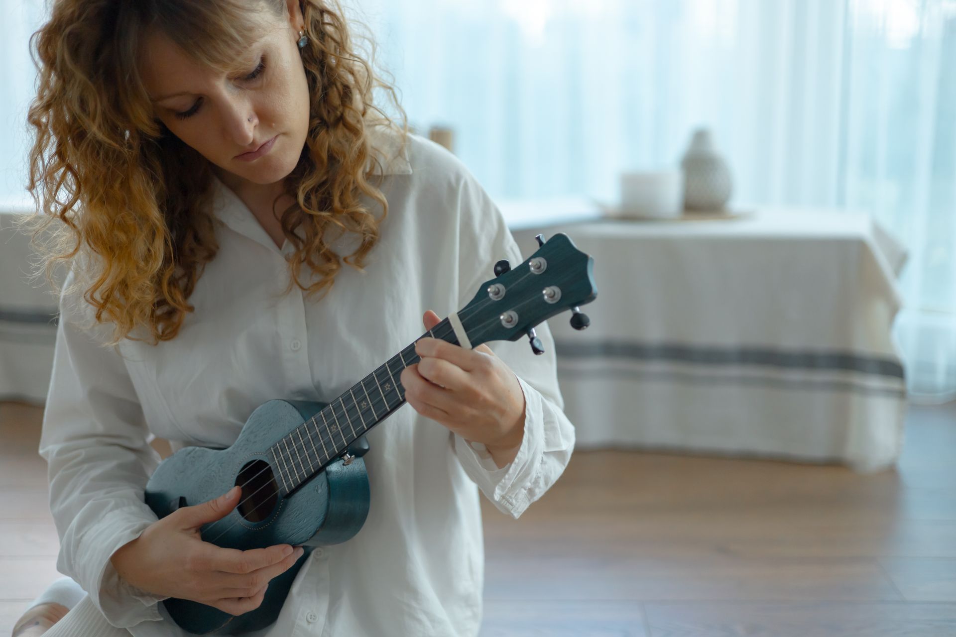 A woman is sitting on the floor playing a ukulele.