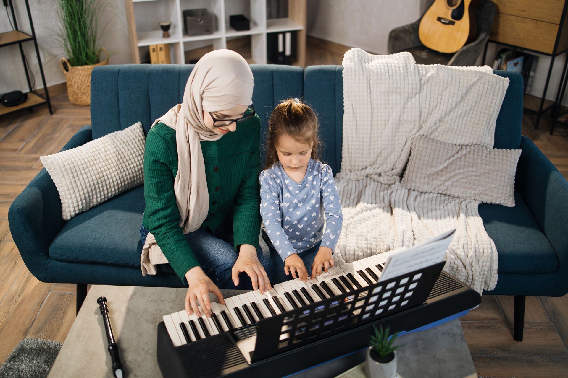 A woman and a little girl are sitting on a couch playing a piano.