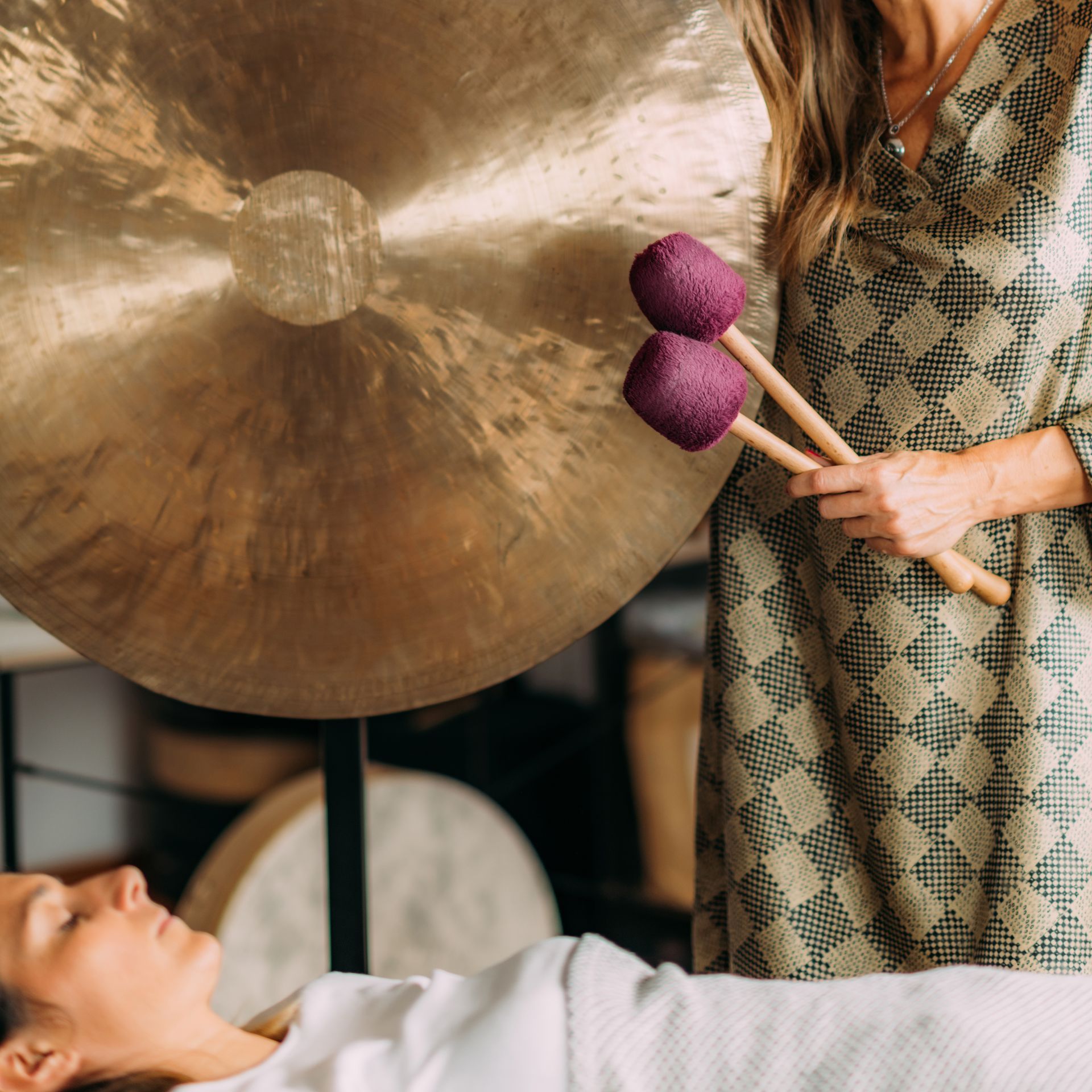 A woman is playing a gong with purple mallets