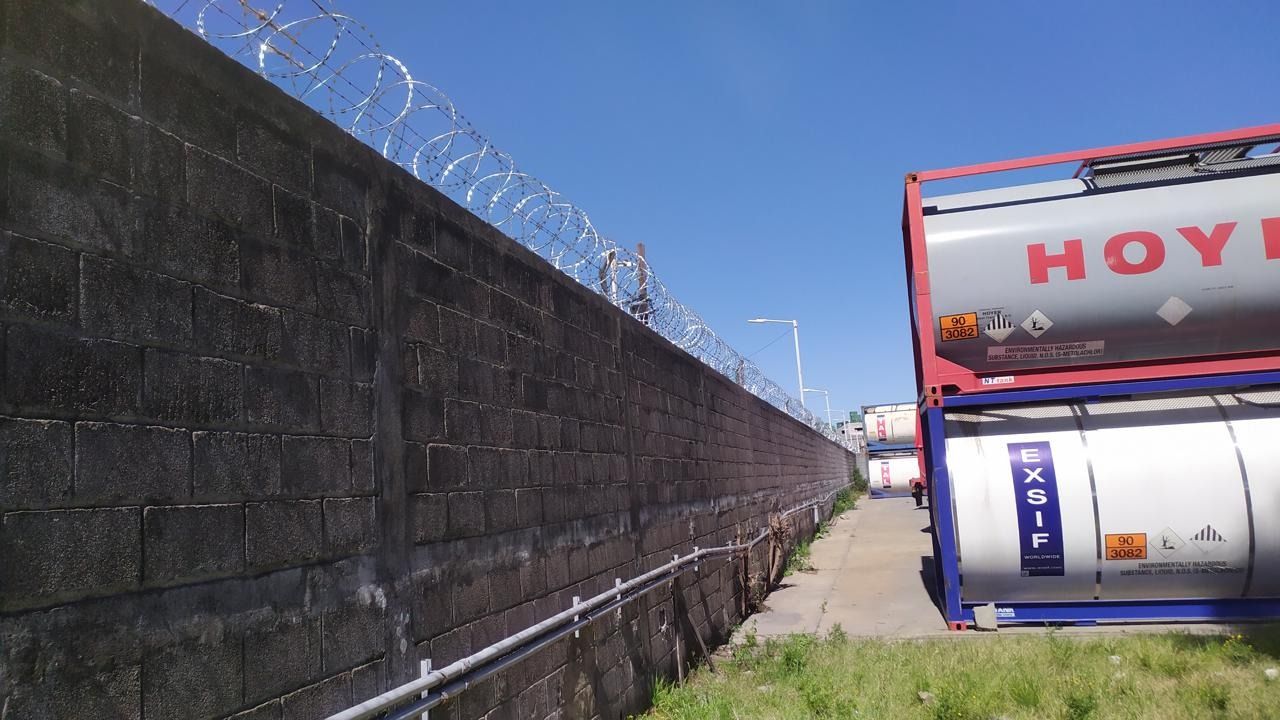 Muro de hormigón con alambre de púas, junto a un camión cisterna, al aire libre en un día soleado.