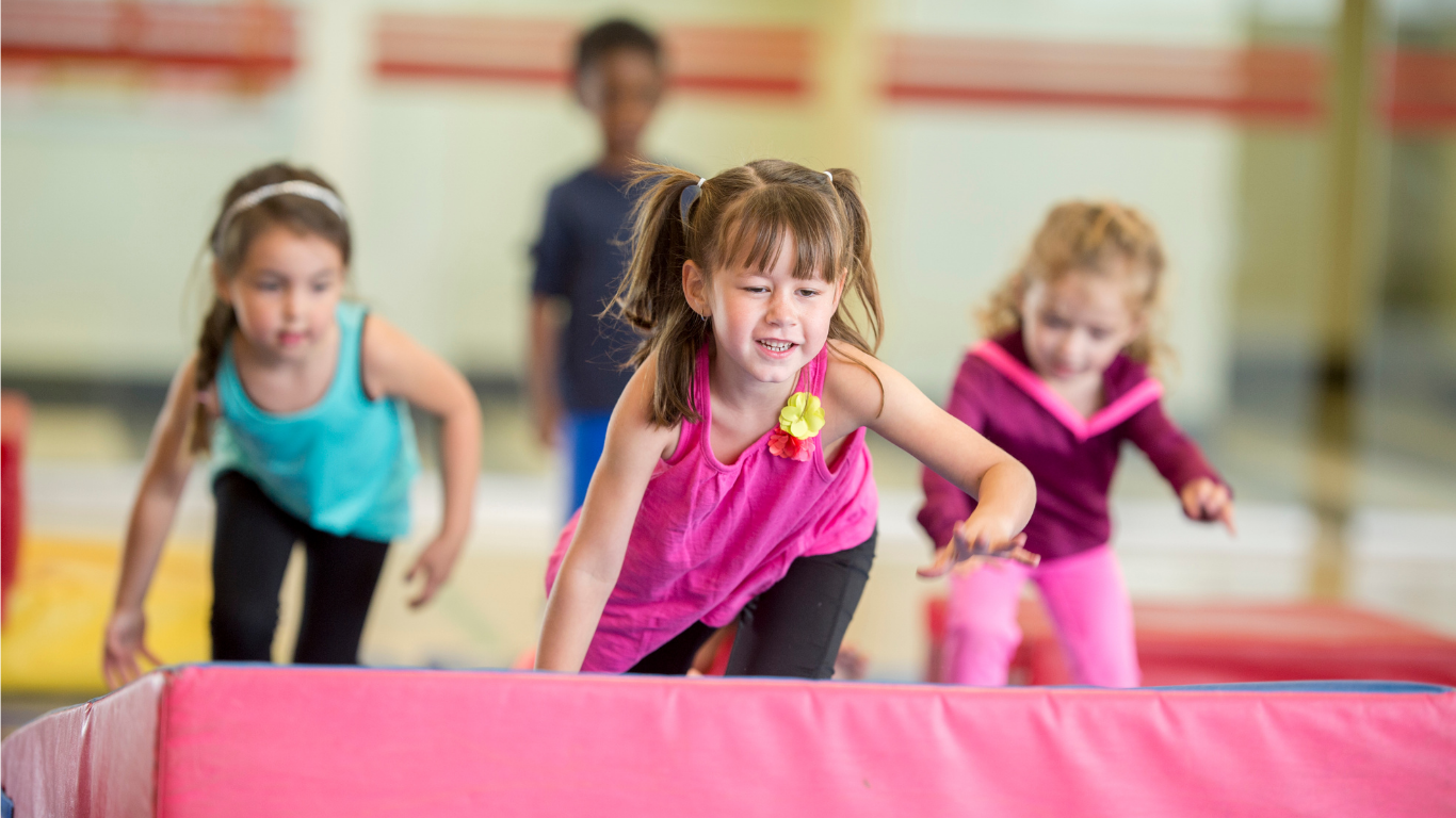 A group of young girls are playing on a balance beam in a gym.