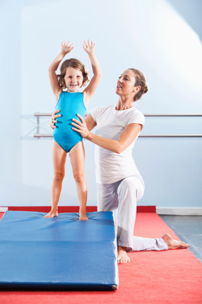 A woman is kneeling next to a little girl on a mat.