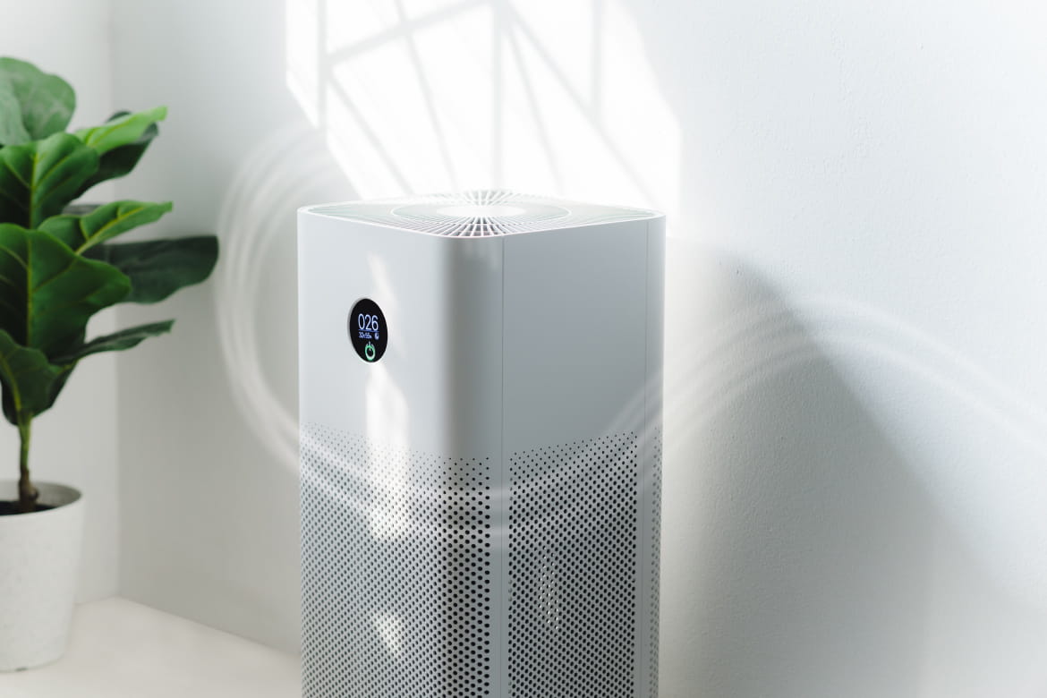 A white air purifier is sitting on a table next to a potted plant.