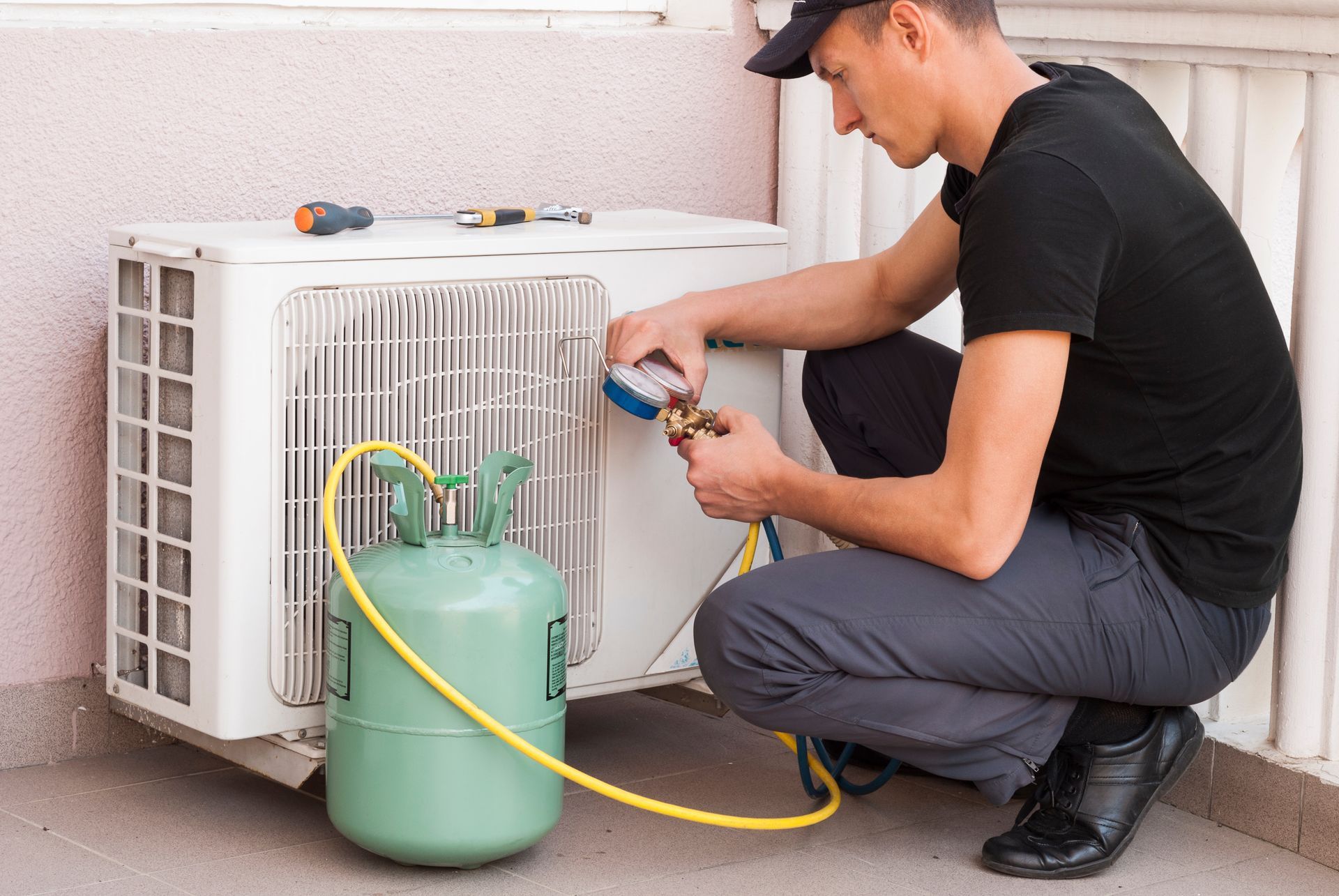 A man is working on an air conditioner on a balcony.