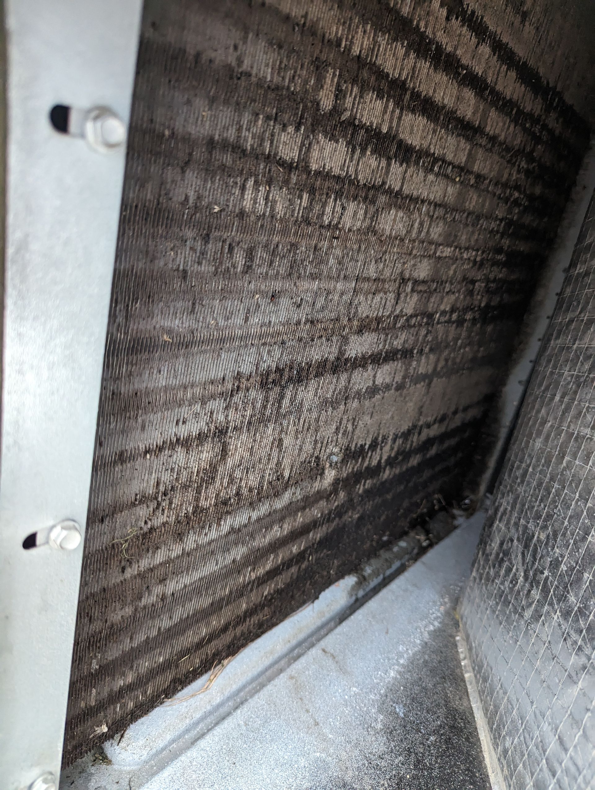 A person is holding a dirty air filter in front of an air conditioner.