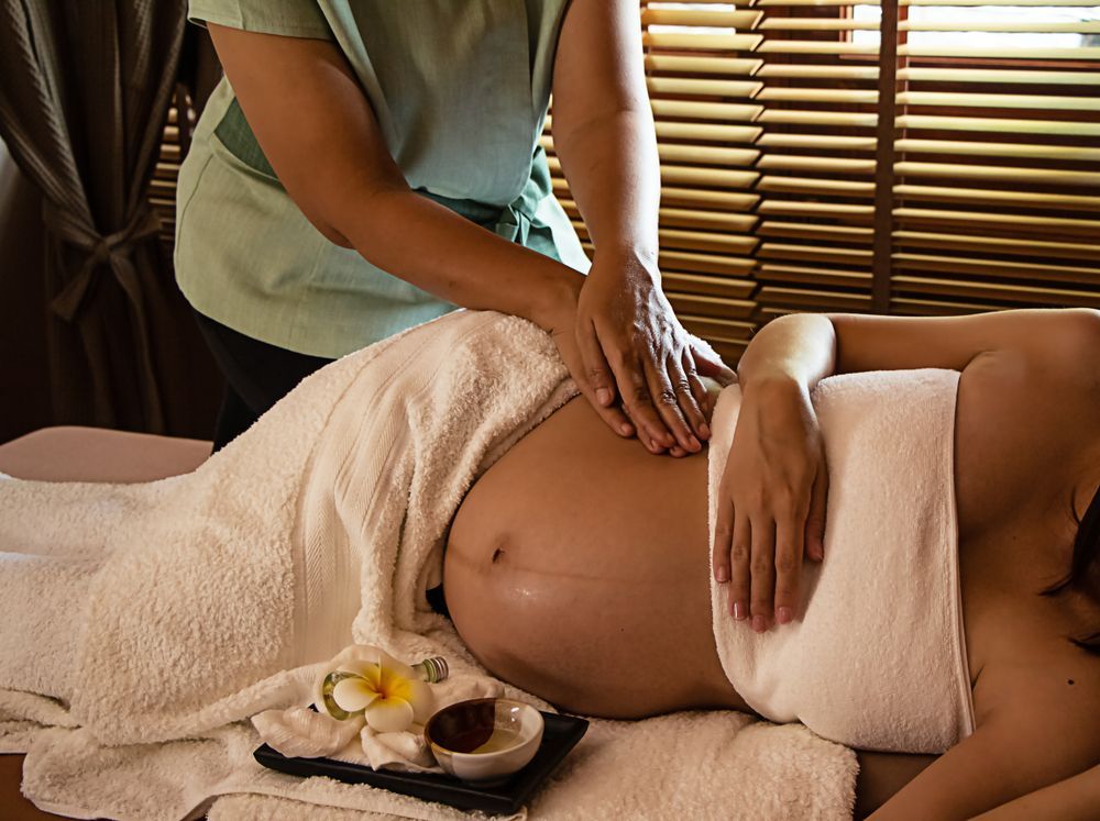 Pregnant person receiving belly massage, lying on a white towel.