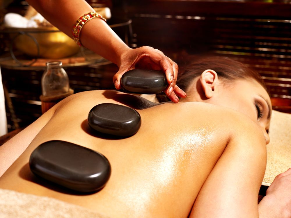 Person receiving hot stone massage on back; stones placed by hand.