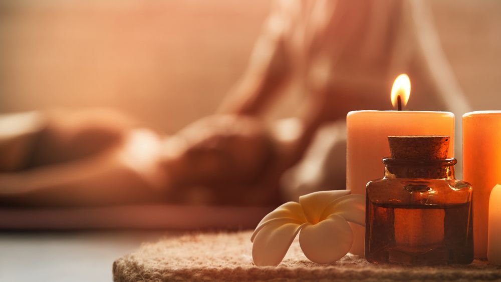 Candles, oil bottle, and flower near person receiving massage.