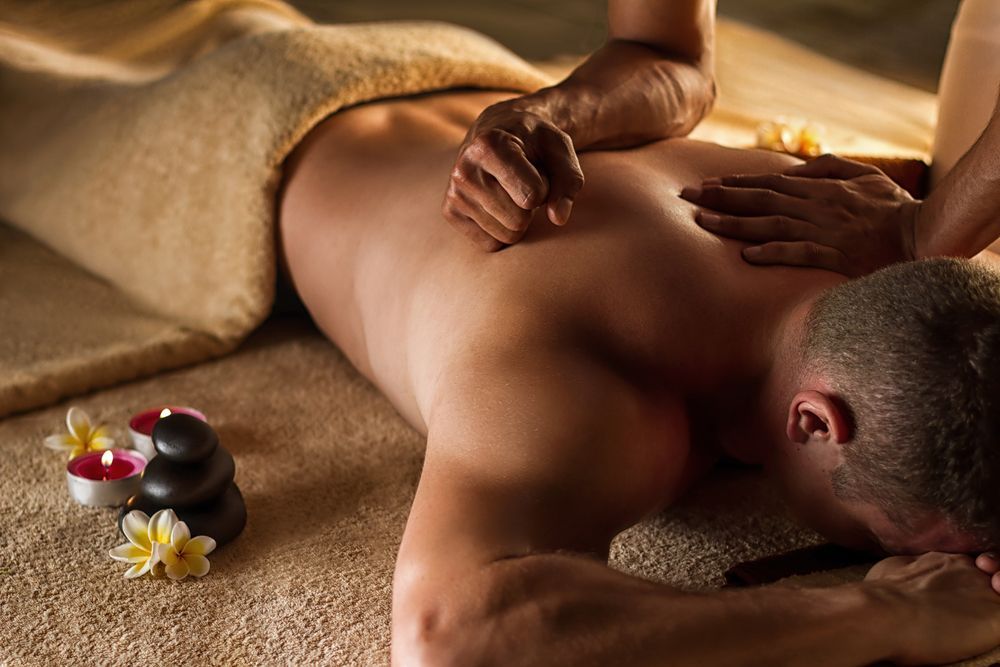 Man receiving a back massage in a spa setting with candles and flowers.