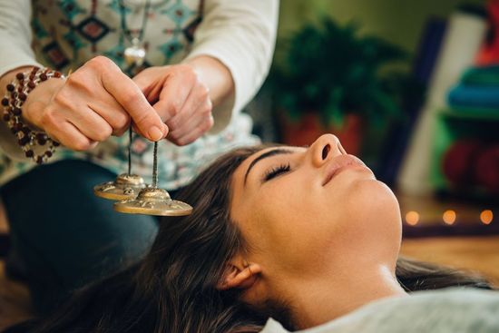 Woman receiving sound healing with small cymbals, eyes closed, in a relaxed setting.