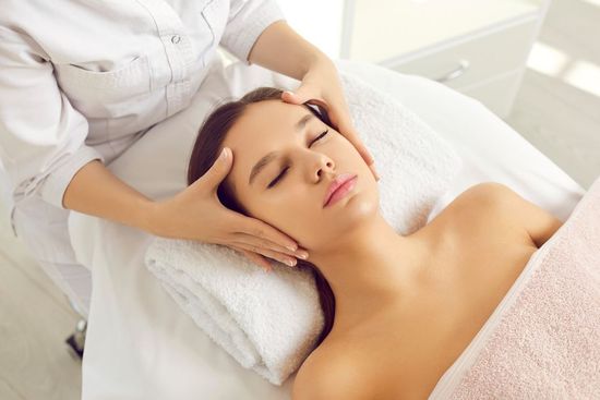 Woman receiving a facial massage at a spa; hands on her face.