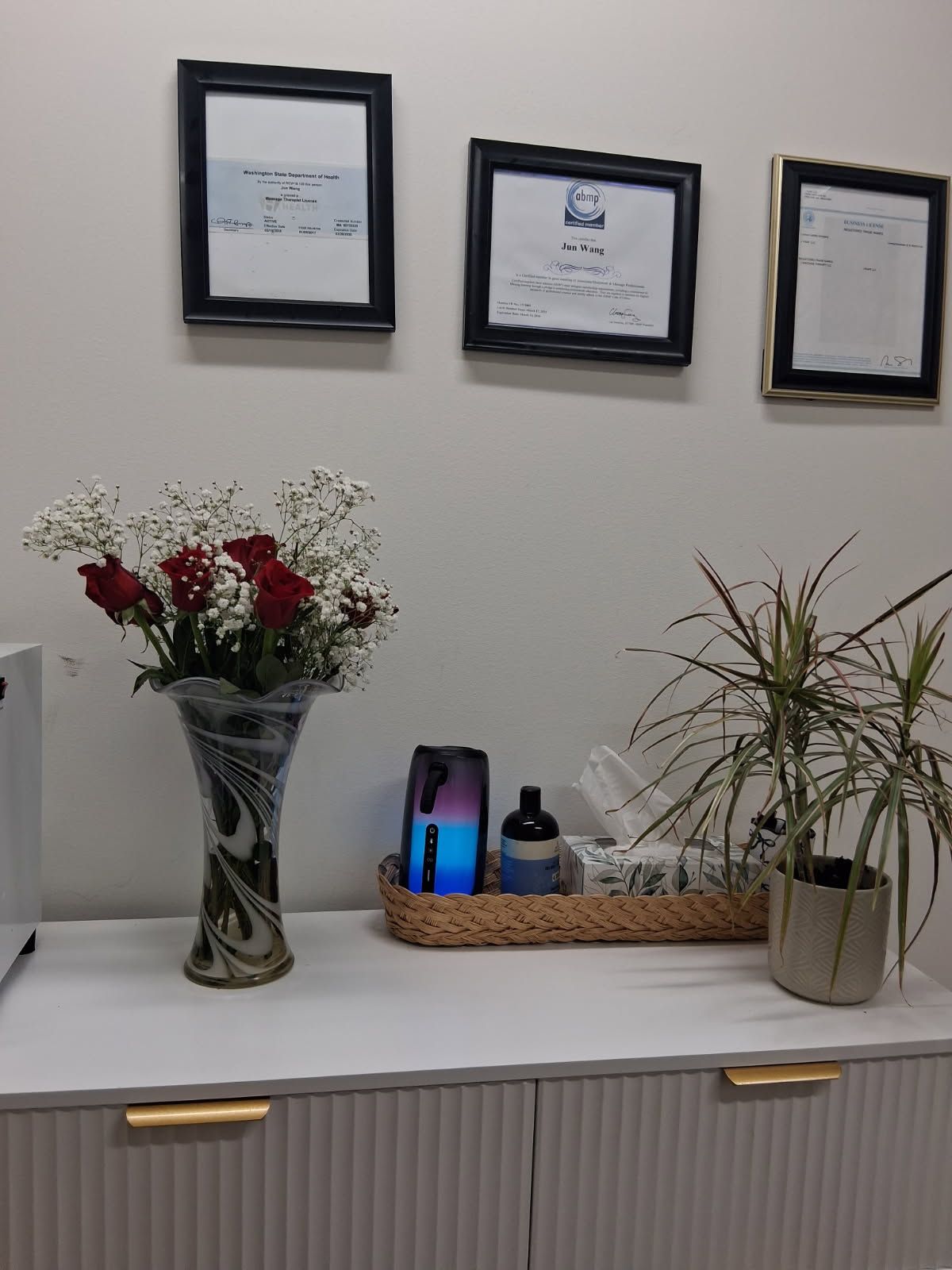 A vase of red roses, framed documents, and decorative items sit on a white cabinet against a white wall.