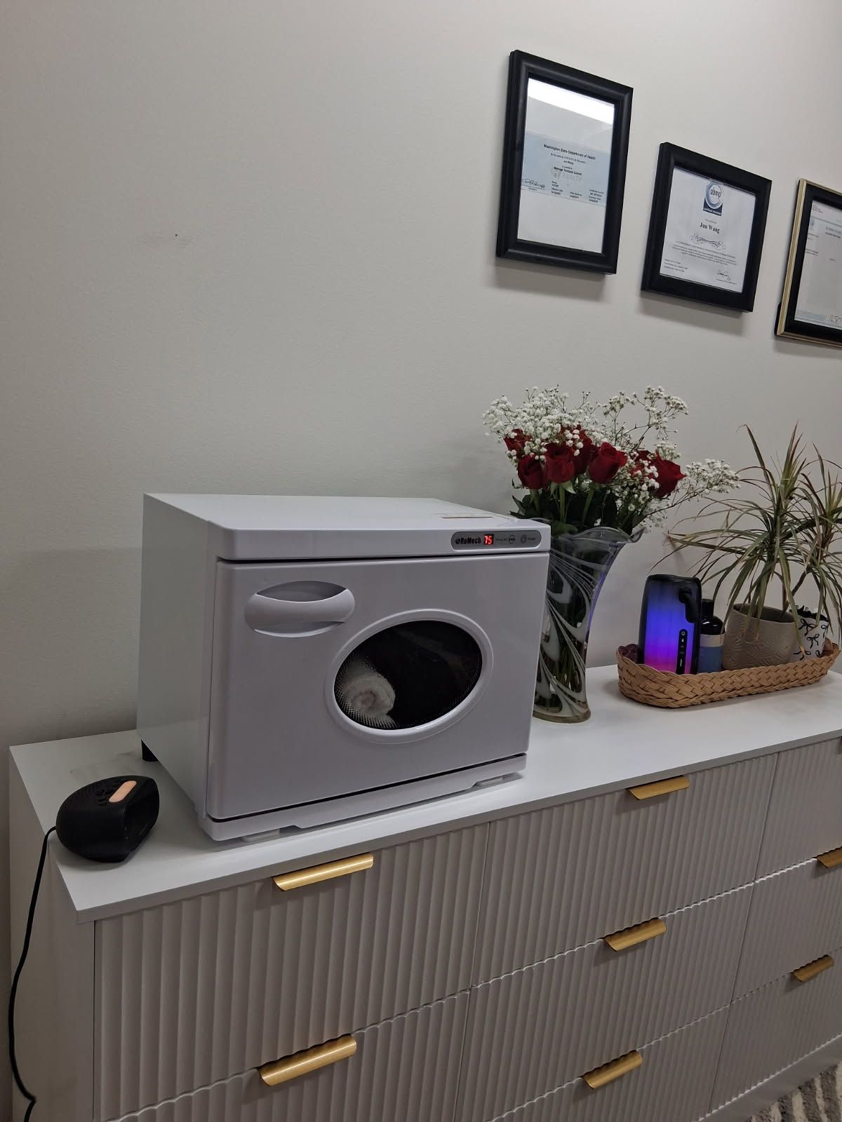 White towel warmer on a dresser with flowers, artwork, and decor.