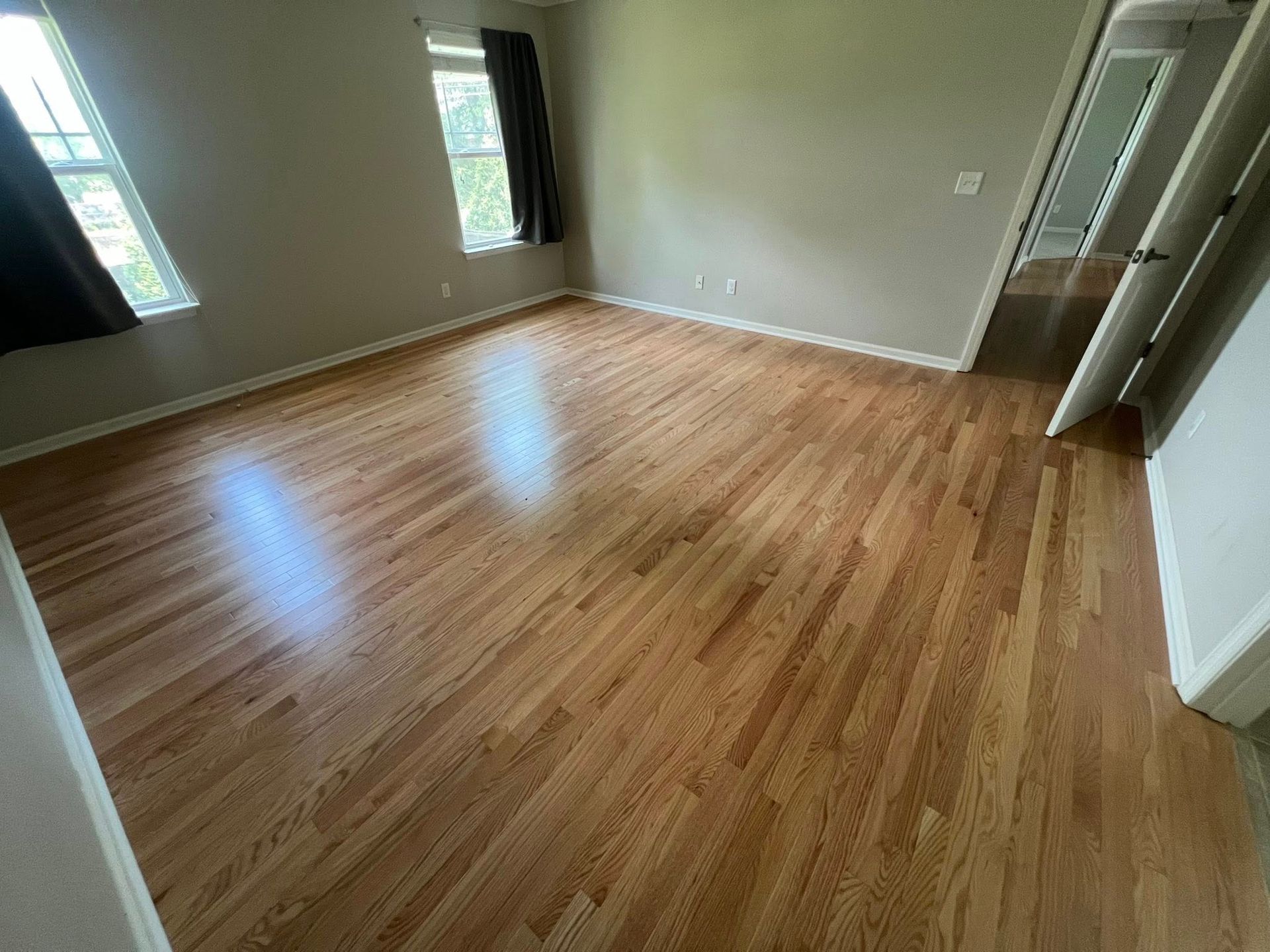 An empty room with hardwood floors and two windows.