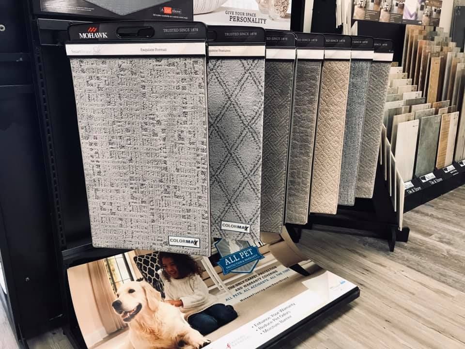 A dog is sitting on a carpet display in a store.