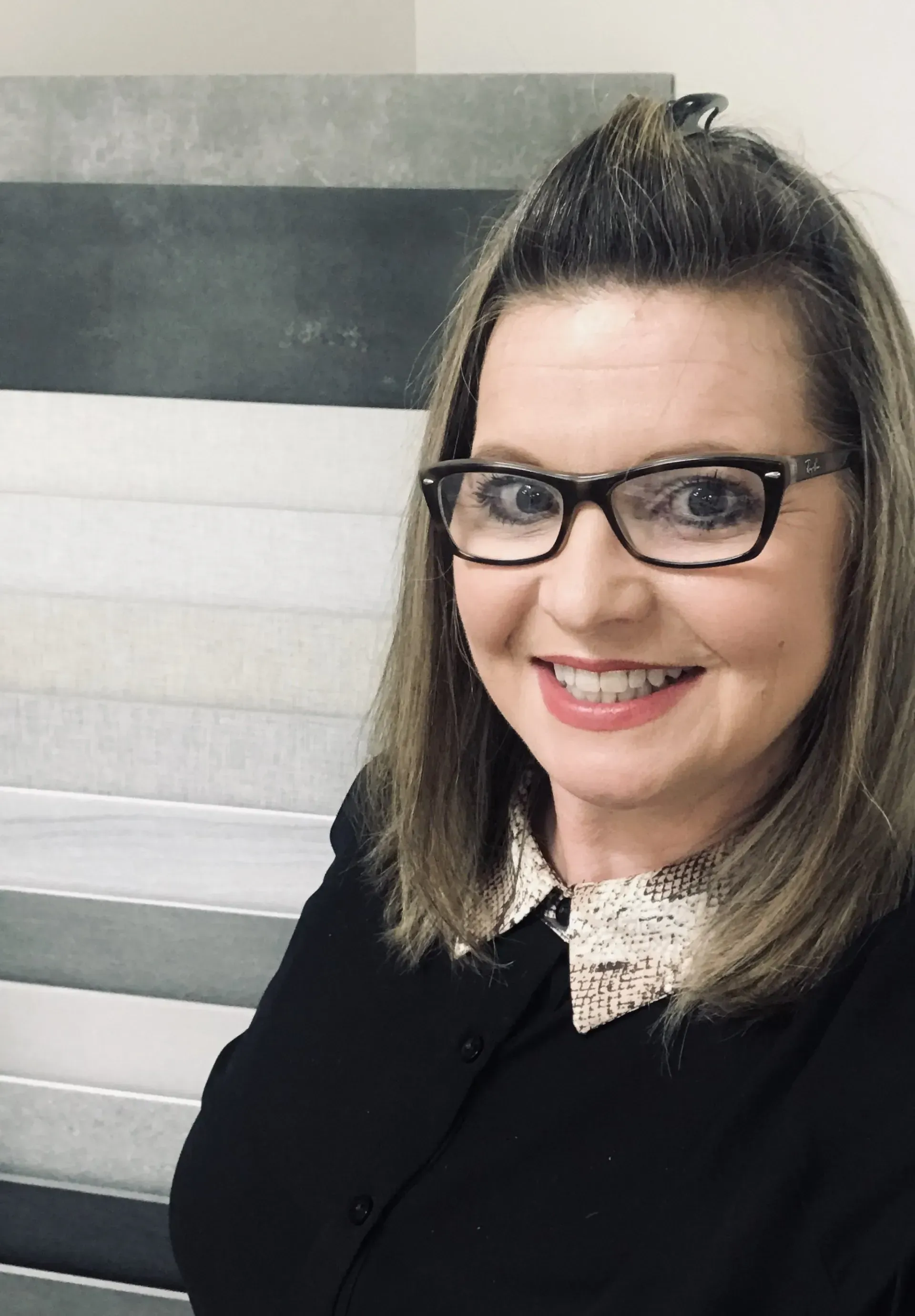 A woman wearing glasses and a black shirt is smiling for the camera.