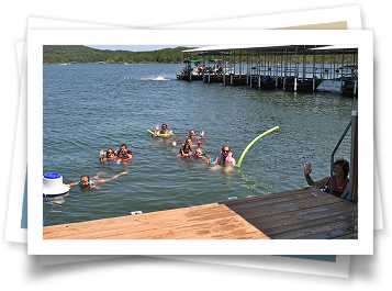 A group of people are swimming in a lake near a dock.