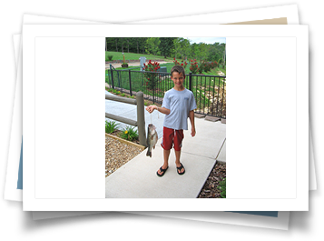 A young boy is standing on a sidewalk holding a fish