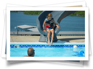 A little girl is sitting on a slide in a swimming pool.