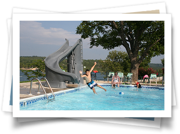 A boy is jumping into a swimming pool with a water slide in the background.