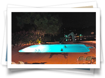 Two people are swimming in a swimming pool at night