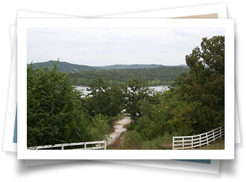 A picture of a dirt road surrounded by trees and a white fence