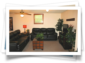 A living room with black leather couches and a ceiling fan