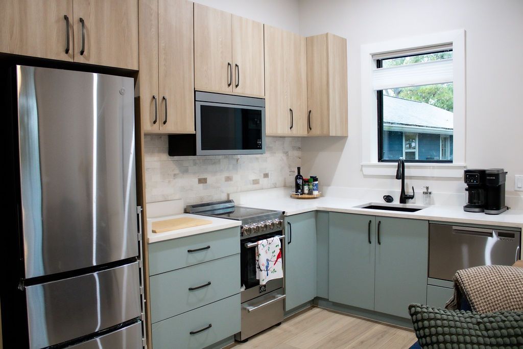 Small kitchen with light wood and teal cabinets, stainless steel appliances, and a small window.