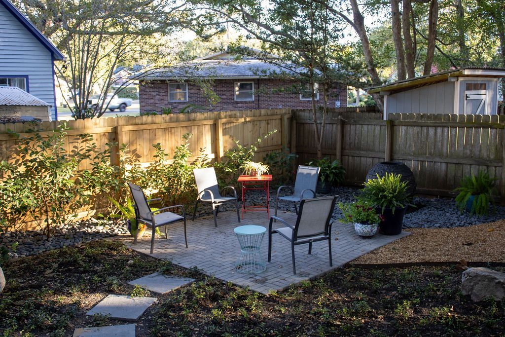 A backyard with a fence , chairs , tables and a fire pit.