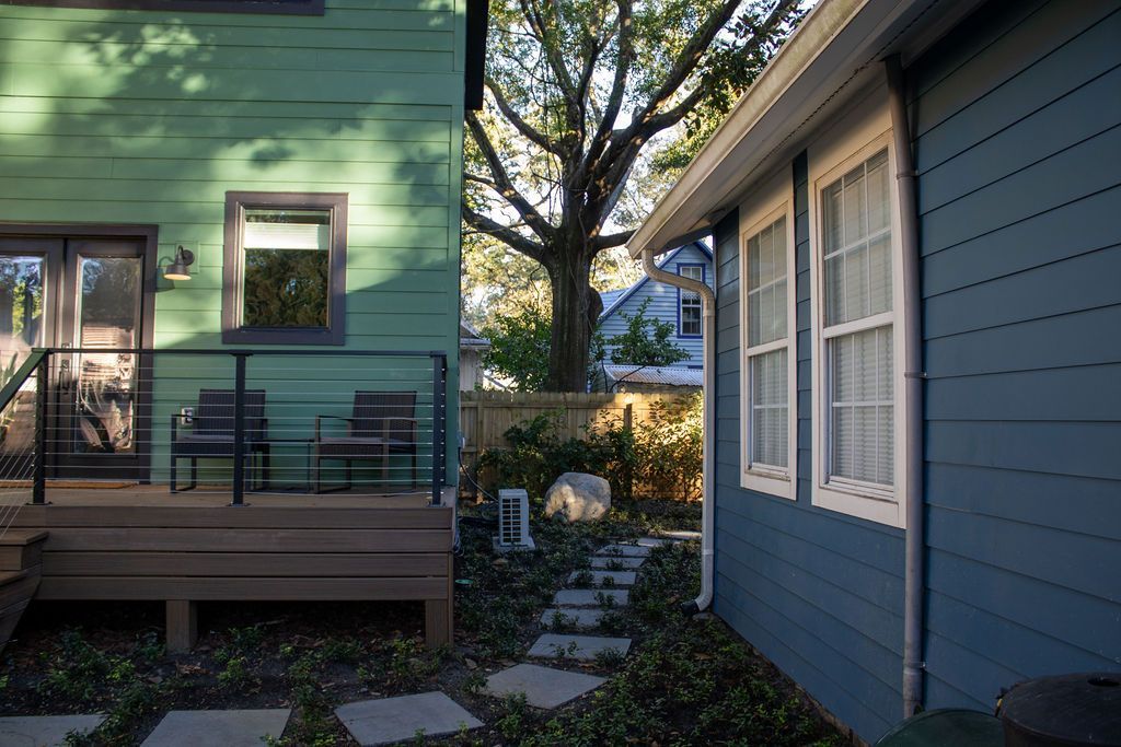 Backyards of two houses, one green with a deck, the other blue, connected by a stone path.