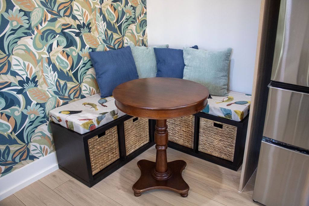 Built-in corner bench with cushions, round table, and storage baskets. Floral wallpaper, blue pillows.