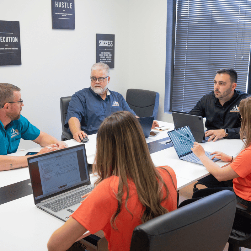 A group of people are sitting around a table with laptops.