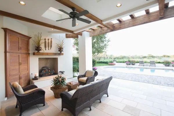 a patio with a fireplace, chairs, a couch and a ceiling fan
