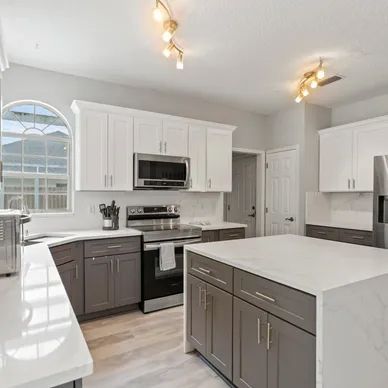 a kitchen with gray cabinets, white counter tops, stainless steel appliances and a large island