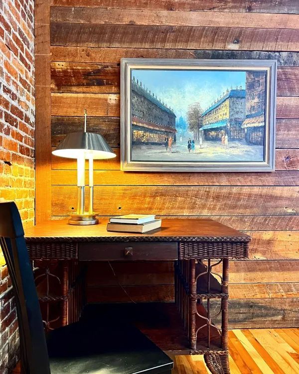a desk with a lamp and a painting on the wall above it