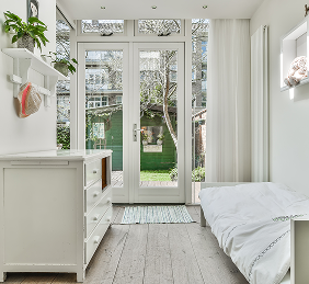 White bedroom with a dresser, bed, and French doors leading to a backyard.