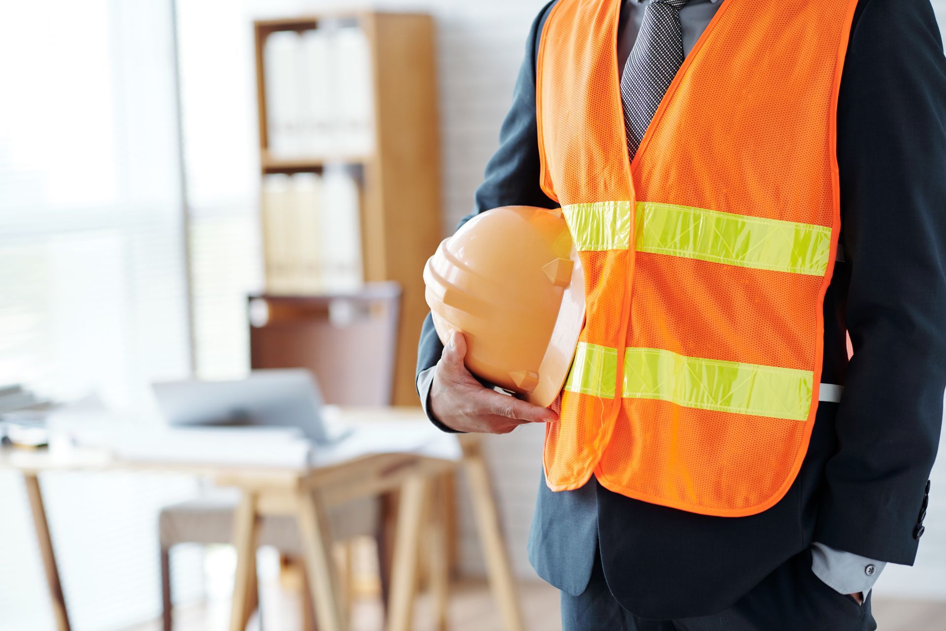 a man in a suit and orange vest is holding a hard hat.