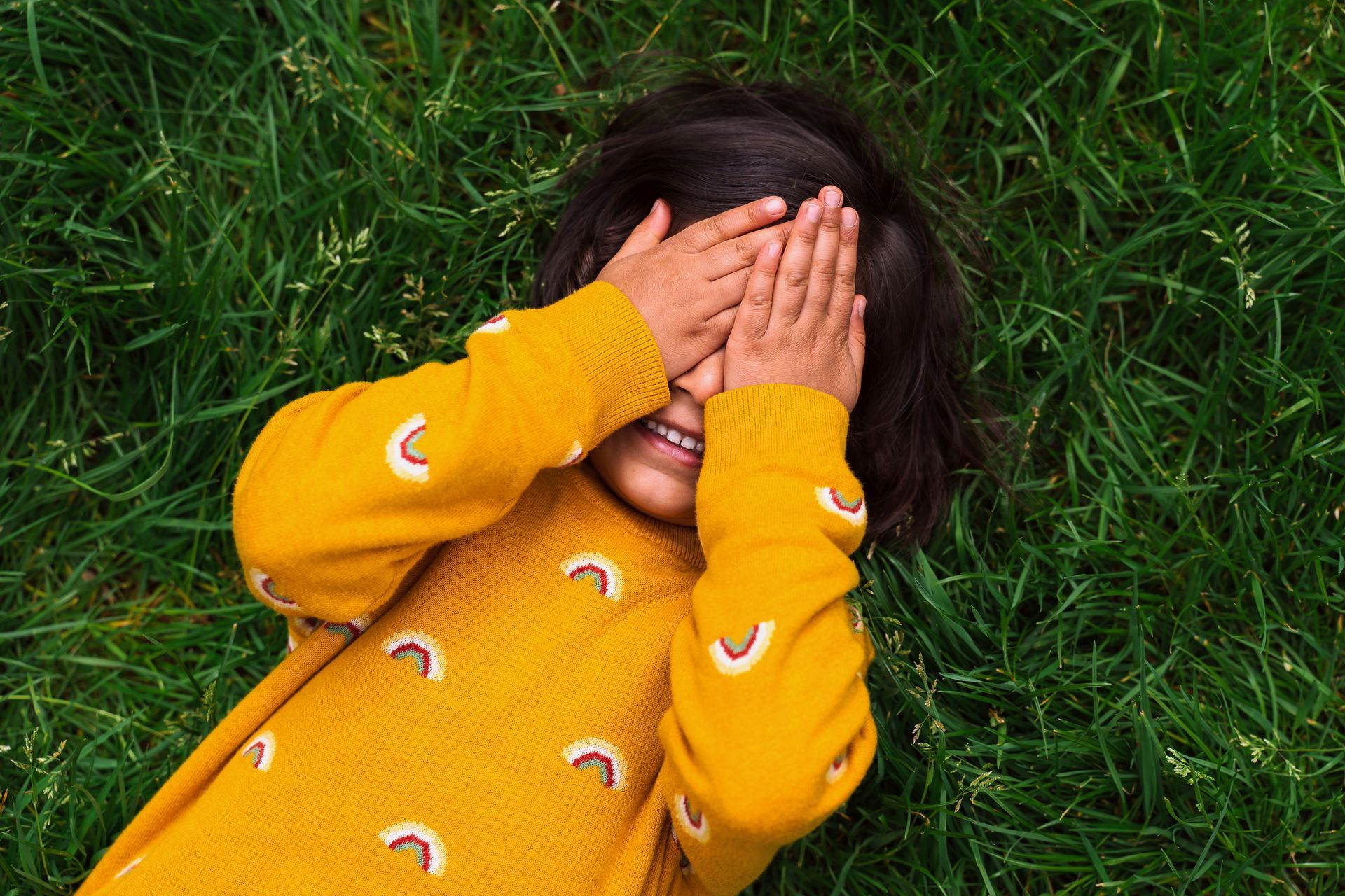 birds eye view of a boy lying on grass with both hands over his eyes